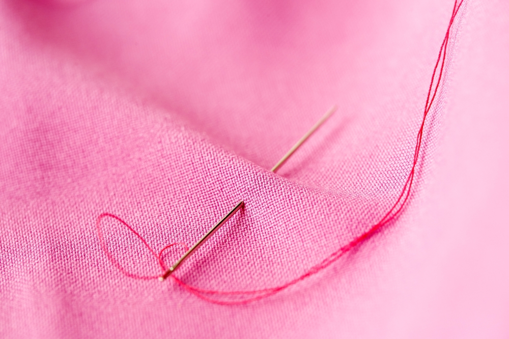 needlework and tailoring concept - sewing needle with thread stuck into pink fabric. sewing needle with thread stuck into pink fabric