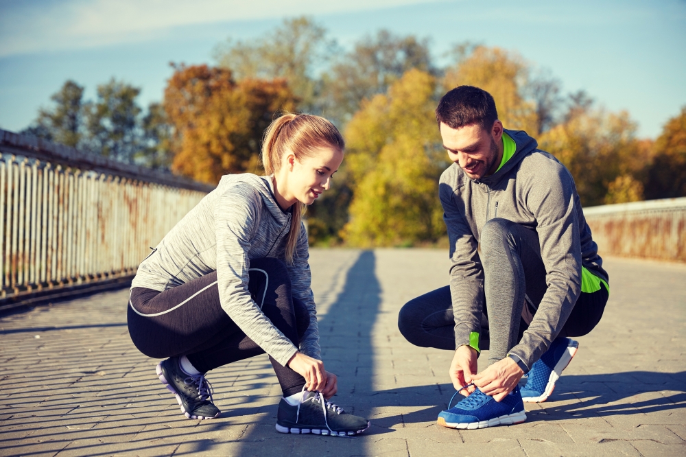 fitness, sport, training, people and lifestyle concept - smiling couple tying shoelaces of sneakers outdoors. smiling couple tying shoelaces outdoors