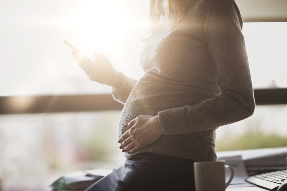 pregnancy, business, work and technology concept - pregnant businesswoman with smartphone and mug at office table. pregnant businesswoman with smartphone at office. pregnant businesswoman with smartphone at office