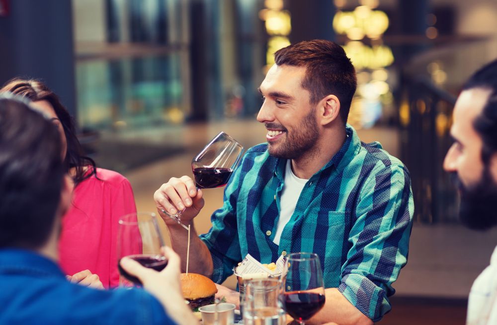 leisure, eating, food and drinks, people and holidays concept - smiling friends having dinner and drinking red wine at restaurant. friends dining and drinking wine at restaurant
