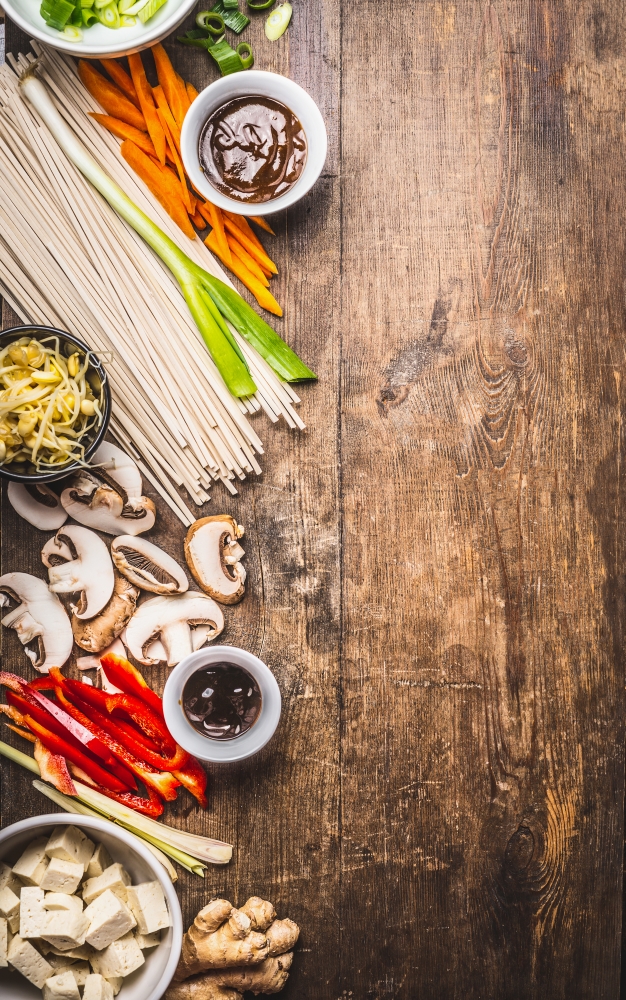 Various asian cuisine ingredients with  tofu, noodles , spices, vegetables and sauces for tasty vegetarian cooking on rustic wooden background, top view, place for text