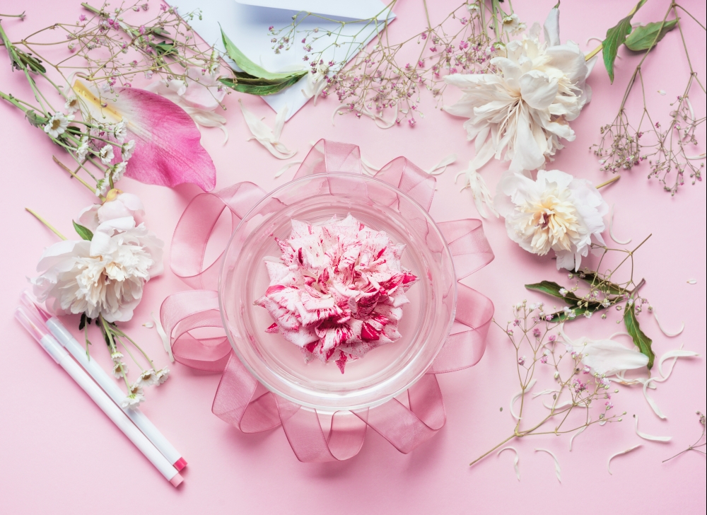 Creative Pink Florist workspace. Pretty floral decoration arrangement with pink roses and plant leaves in glass vase with water and florist decoration equipment, top view. Holiday concept