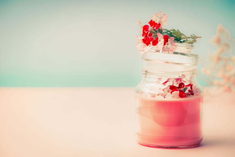 Pink cream in glass jar for skin care  with flowers Stands on the table at turquoise background, front view. Beauty, cosmetic, spa or body care concept