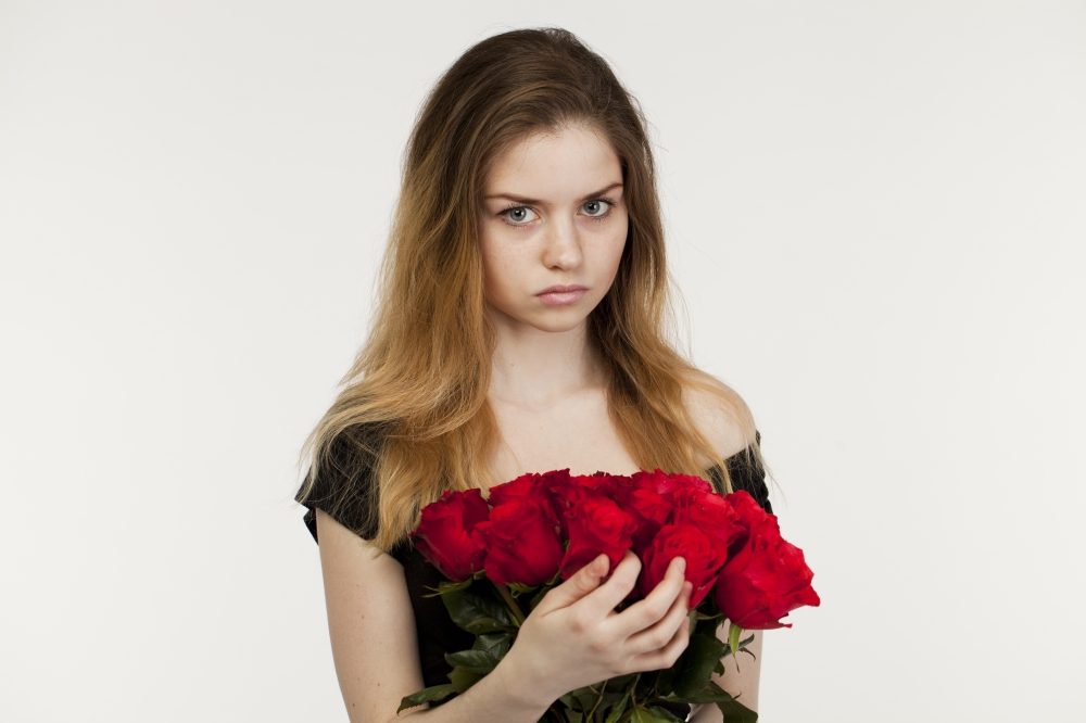 Portrait of a young beautiful blonde girl with a bouquet of red roses, isolated on white background