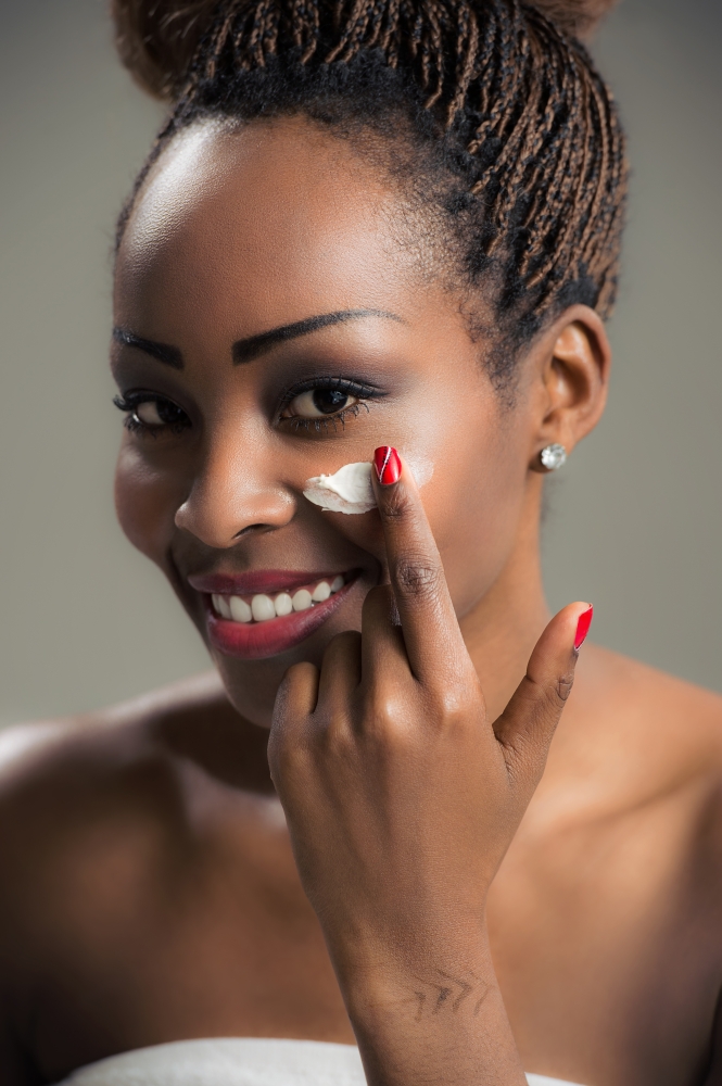 Beauty face of young african american woman with cosmetic cream on a cheek. Skin care concept. Closeup portrait.