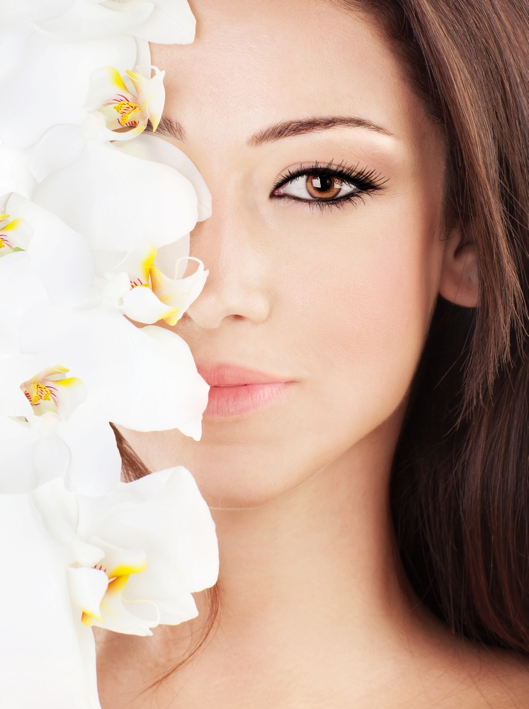 Closeup on beautiful face with white orchid flower, perfect clean skin, young female portrait, beauty and spa concept