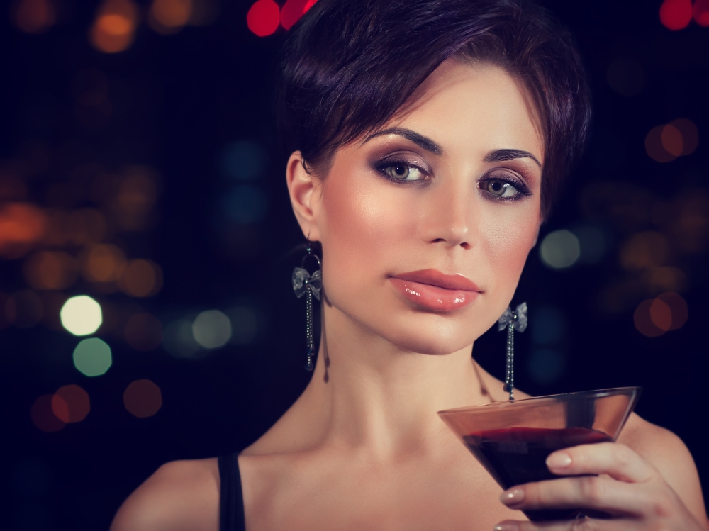 Portrait of beautiful brunet woman on the party, holding in hand glass of martini, spending evening in night club, celebrating New Year