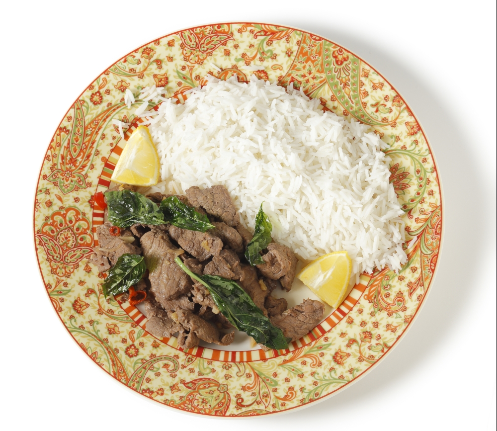 Chilli beef with crispy fried basil leaves, served with white basmati rice and lemon wedges, viewed from above