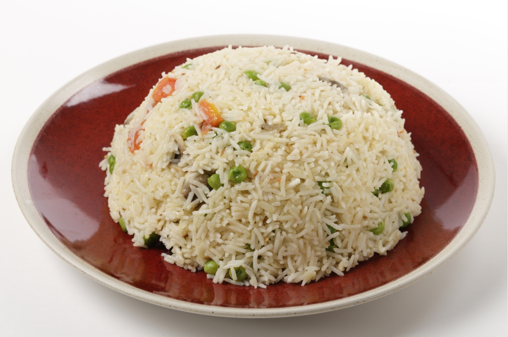 A moulded dome of vegetable pilau rice on a plate ready for serving, made with garlic, sliced mushrooms, chopped tomato, cumin seeds and basmati rice.
