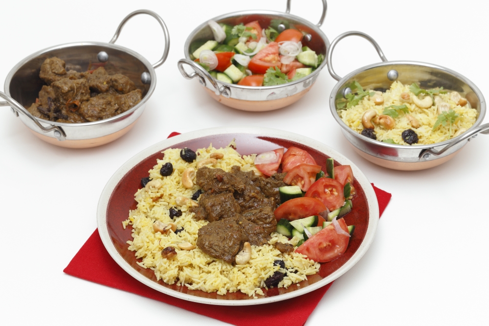 Beef madras curry served with saffron, raisin and roast cashew nut pilau rice and a salad of tomato, cucumber and shallots. Kadai serving bowls with each of the elements are at the back.