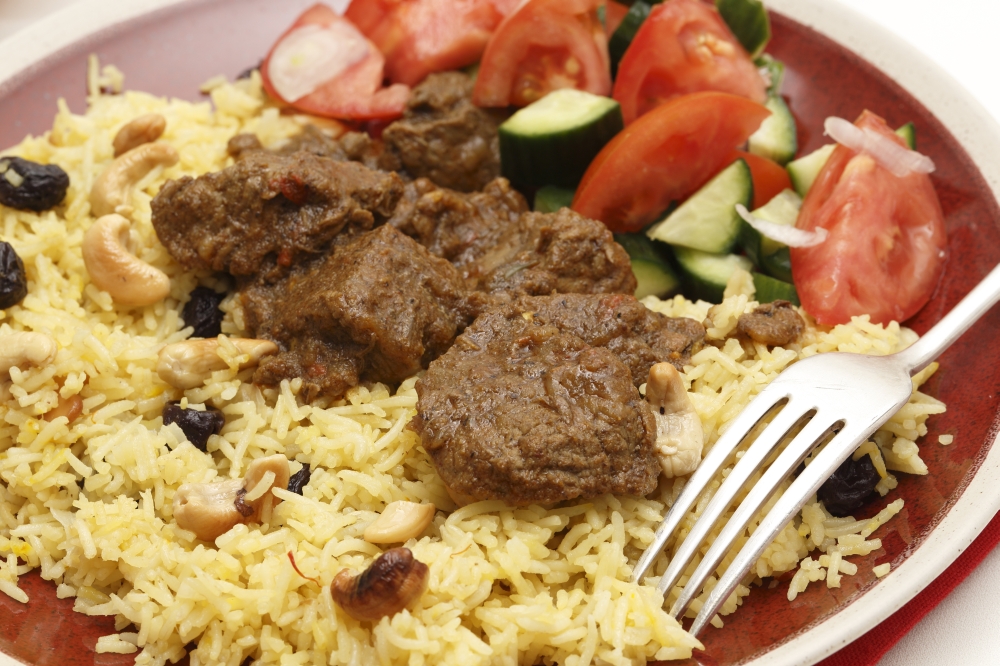 Close-up view of a homemade beef madras curry served with saffron, raisin and roast cashew nut pilau rice and a salad of tomato, cucumber and shallots.