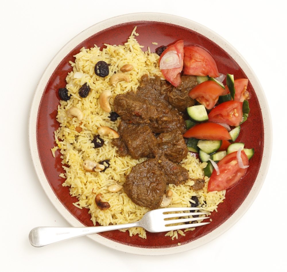High-angle view of a homemade beef madras curry served with saffron, raisin and roast cashew nut pilau rice and a salad of tomato, cucumber and shallots.