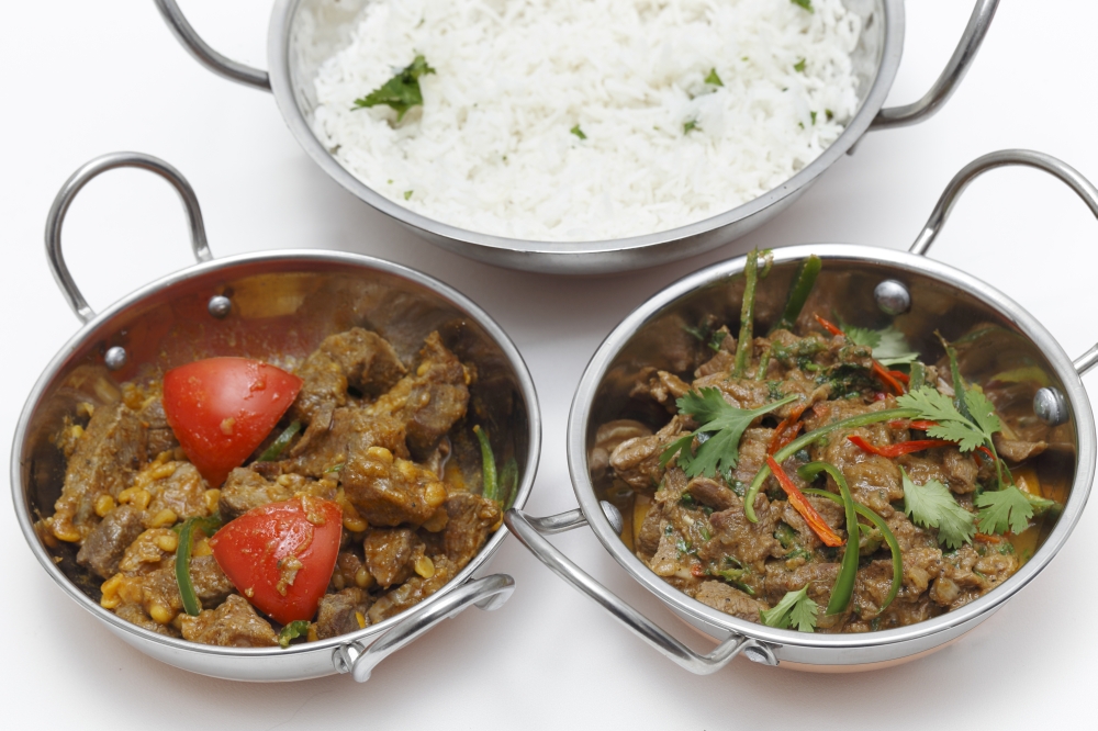 A bowl of spiced lamb curry with coriander leaves and slivers of red and green chillies, next to a bowl of Lahore-style lamb curry with split peas and some rice.