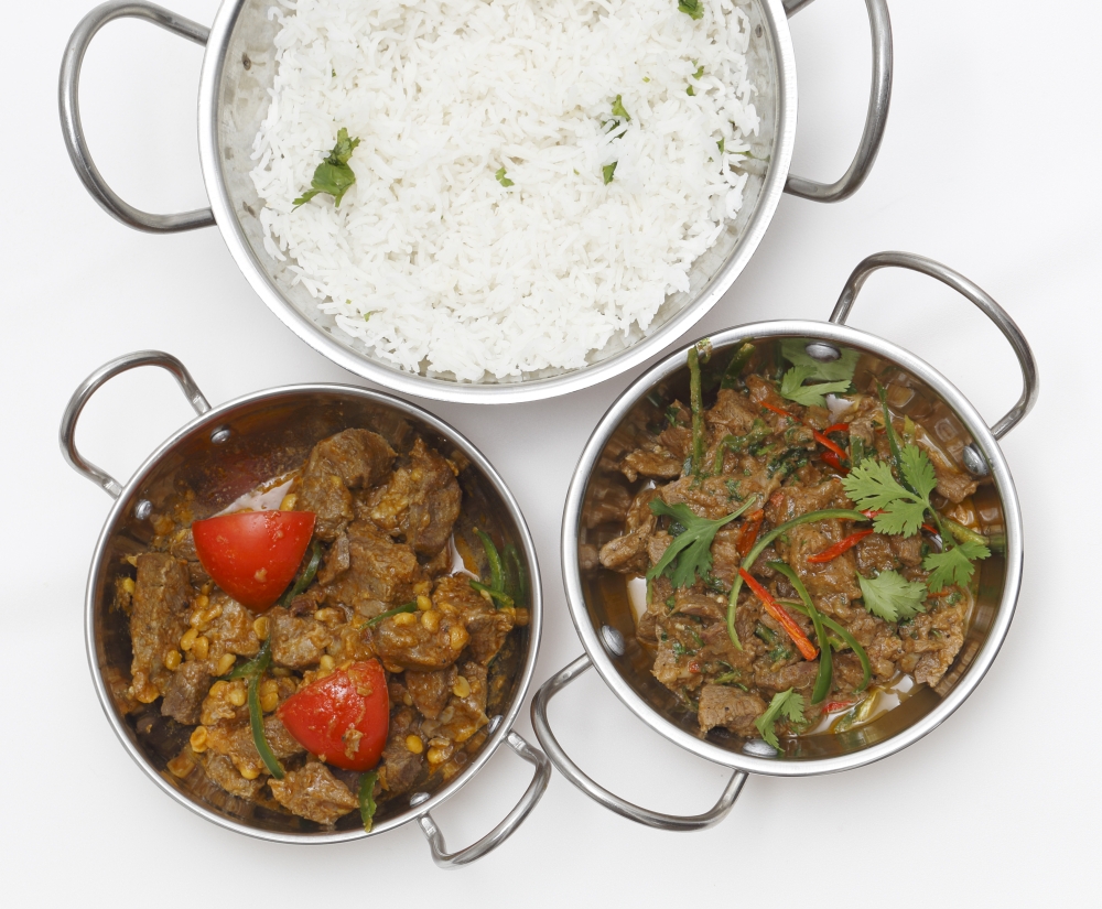 A bowl of spiced lamb curry with coriander leaves and slivers of red and green chillies, next to a bowl of Lahore-style lamb curry with split peas and some basmati rice. from above