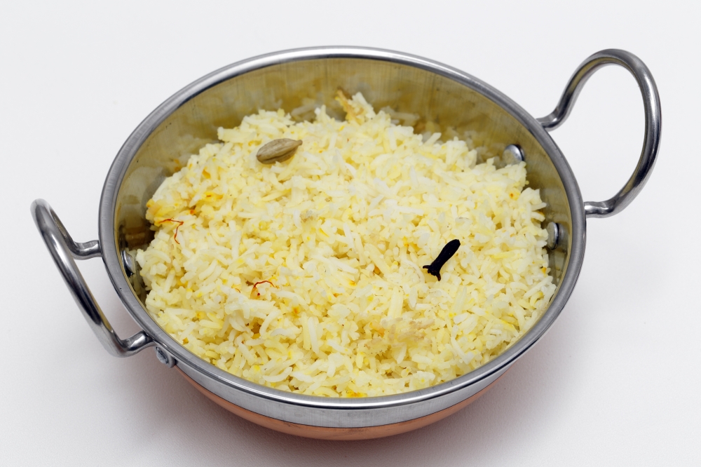 Homemade traditional saffron rice, made with basmati long-grain rice, cardamom pods, cloves and saffron threads, in an Indian kadai or karahi (wok) bowl