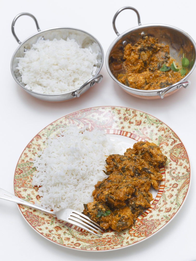 Methi murgh - chicken cooked with fresh fenugreek leaves -  served on a plate with rice with the curry sauce  behind, in a kadai, or karahi, traditional Indian wok,  next to a bowl of basmati rice