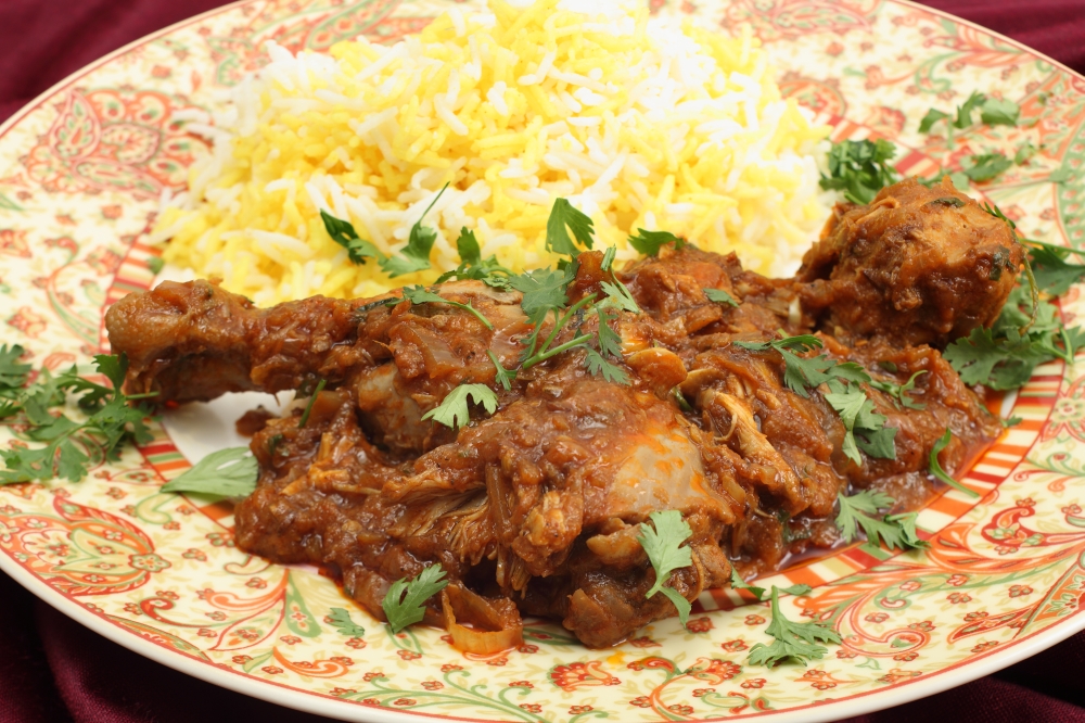Homemade butter chicken masala with yellow and white rice, garnished with chopped coriander leaves.