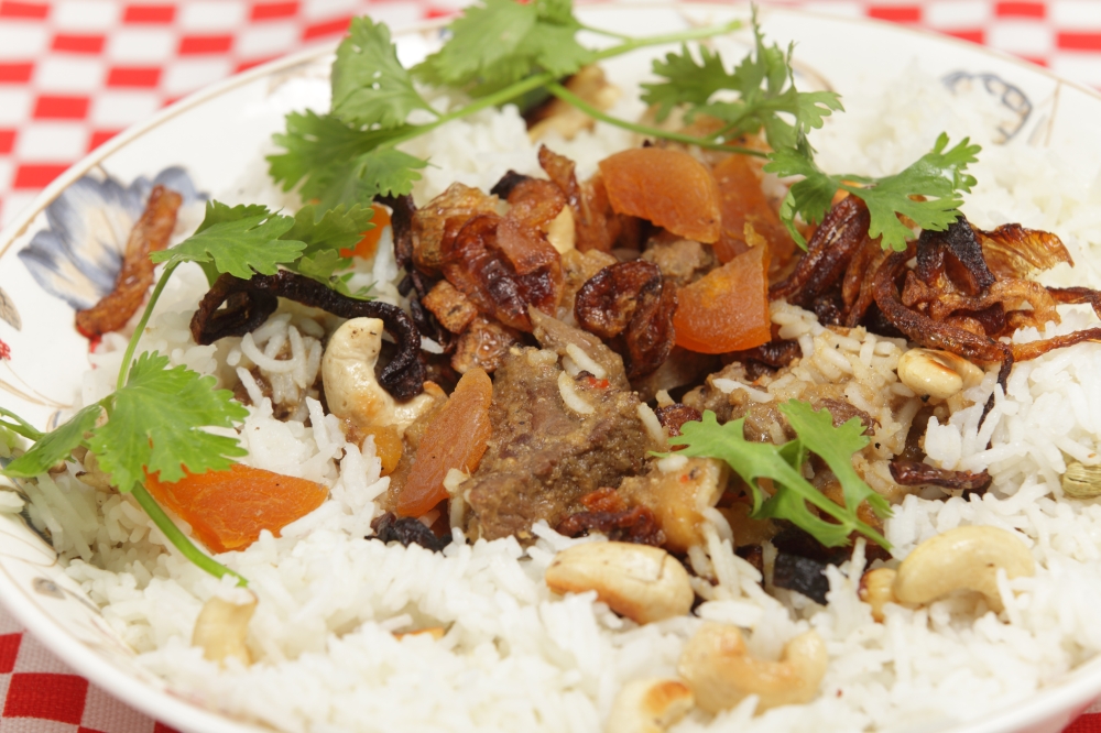 A serving bowl of home-made biryani-type fragrant lamb curry, cooked with dried apricots and yoghurt and garnished with toasted cashews, fried onions and coriander, served with cardamom-flavoured basmati rice.