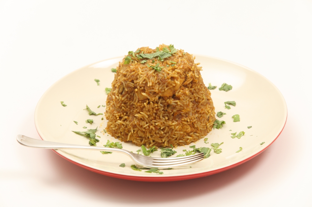 A plate of traditional Indian chicken biryani, garnished with coriander (cilantro) and mint leaves on a plate with a fork