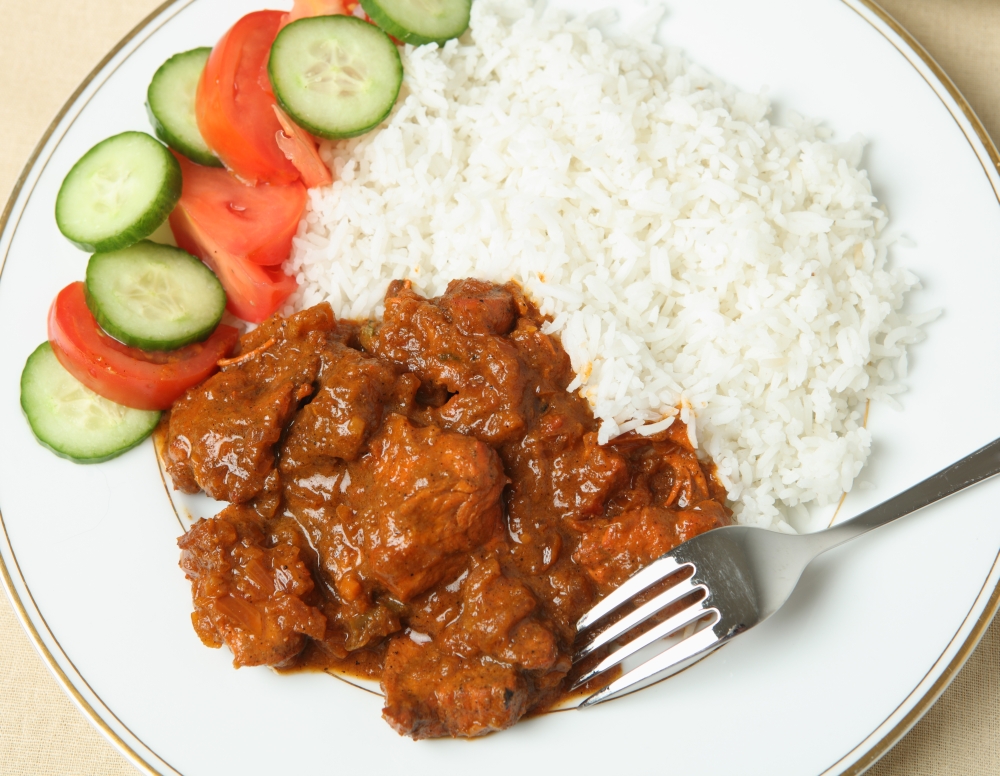 A plate of chicken tikka masala with basmati rice and a salad of cucumber and tomato.