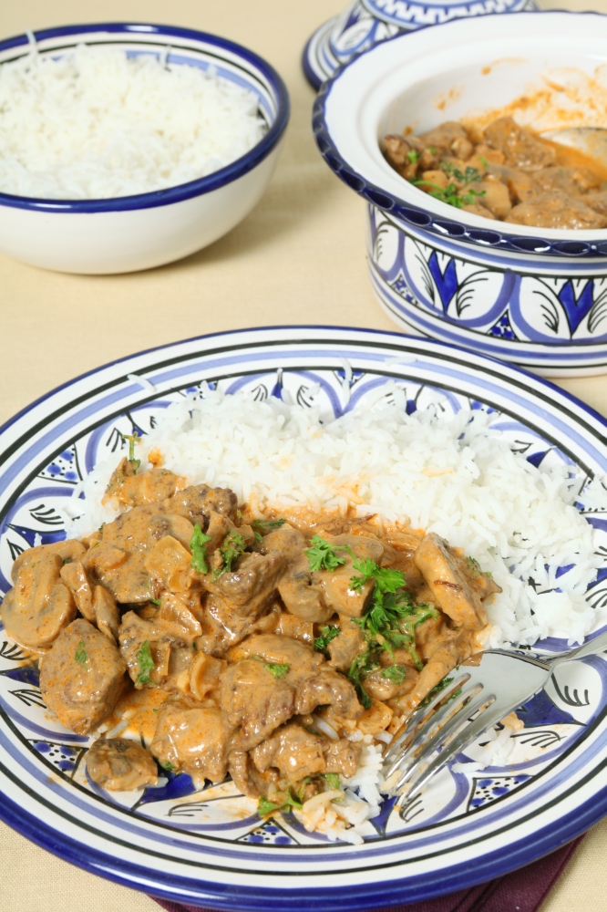 A meal of beef stroganoff with white rice and a fork on a table, vertical orientation