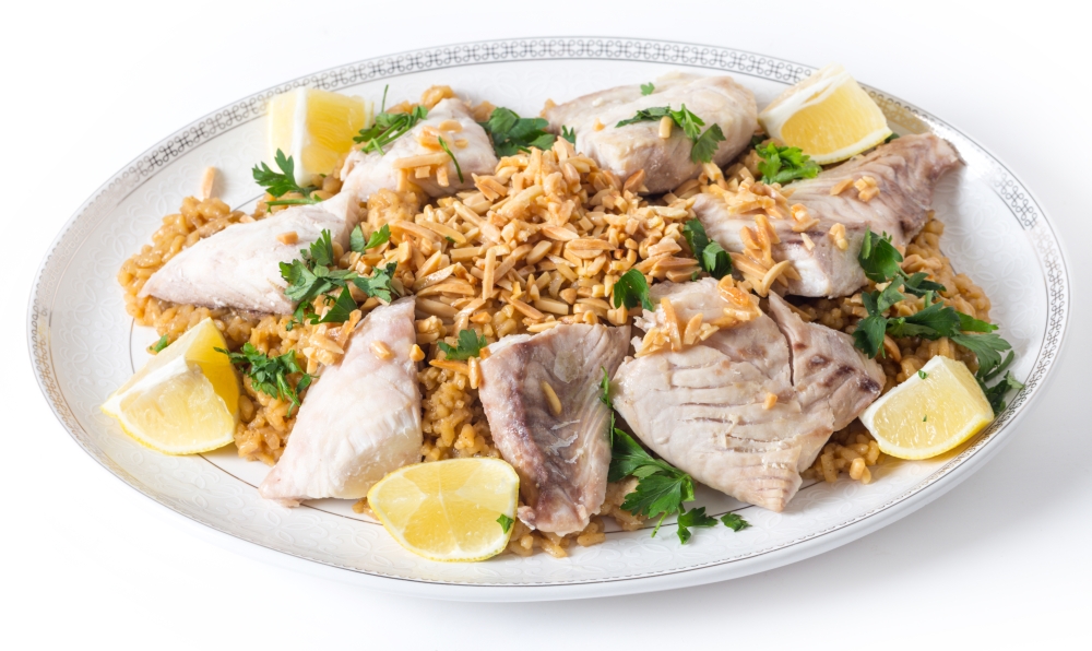 Lebaneses-style fried fish on a serving dish with caramelised onion flavoured rice and roasted almond slivers.