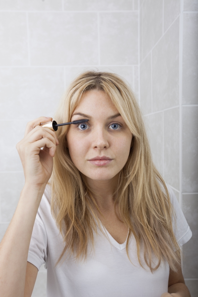 Portrait of young woman applying mascara in bathroom