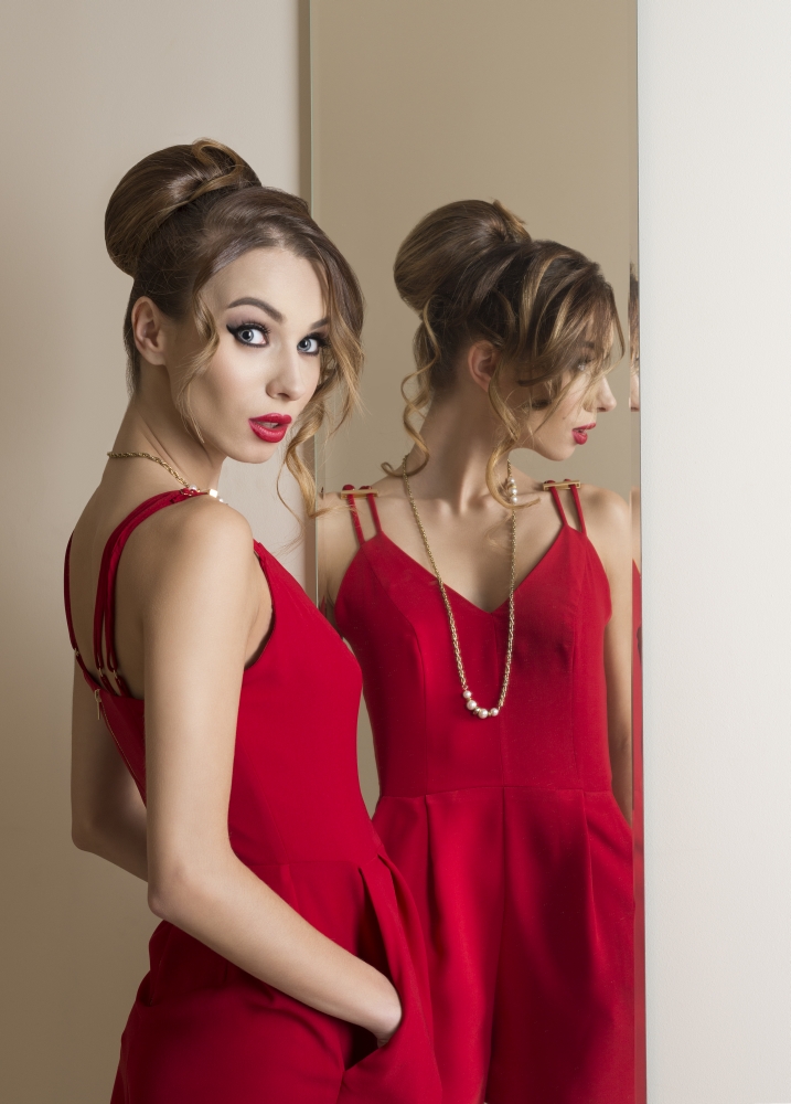fashion woman with hairdo and make-up trying red dress in front or the mirror. Changing room. Shopping time