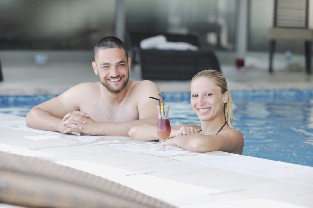happy young couple in love have fun  relax and  drink coctail at indoor wellness swimming pool