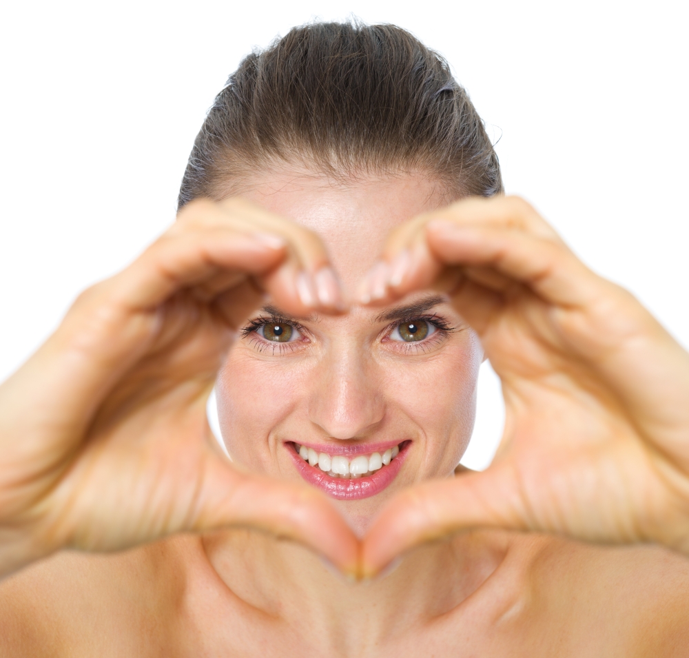 Smiling young woman looking through heart shaped hands