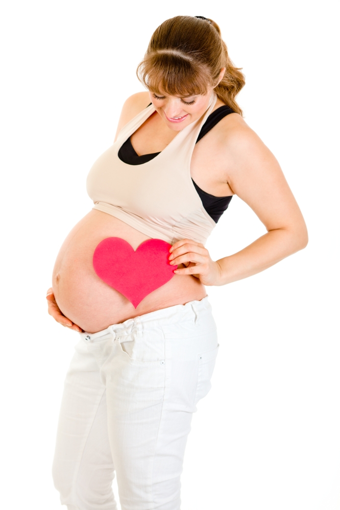 Smiling pregnant woman holding heart near her tummy isolated on white&#xA;