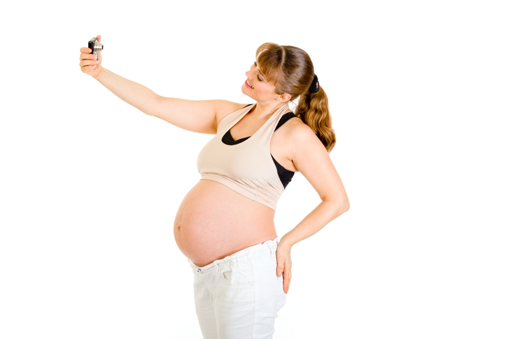 Smiling pregnant woman photographing herself isolated on white&#xA;