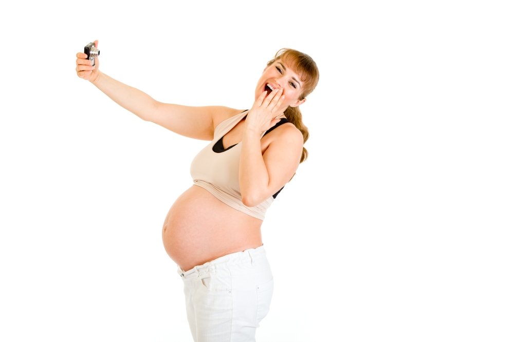 Laughing pregnant woman photographing herself isolated on white&#xA;