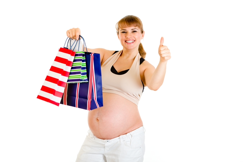 Happy pregnant woman holding shopping bags and showing thumbs up gesture isolated on white&#xA;