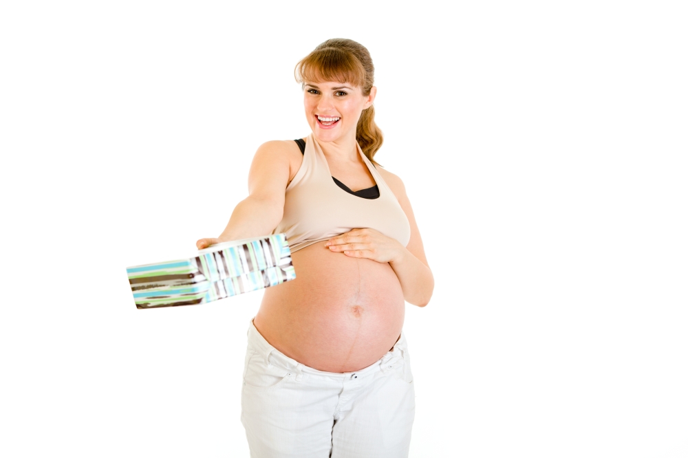 Smiling pregnant woman touching her belly and  holding present for baby  isolated on white&#xA;