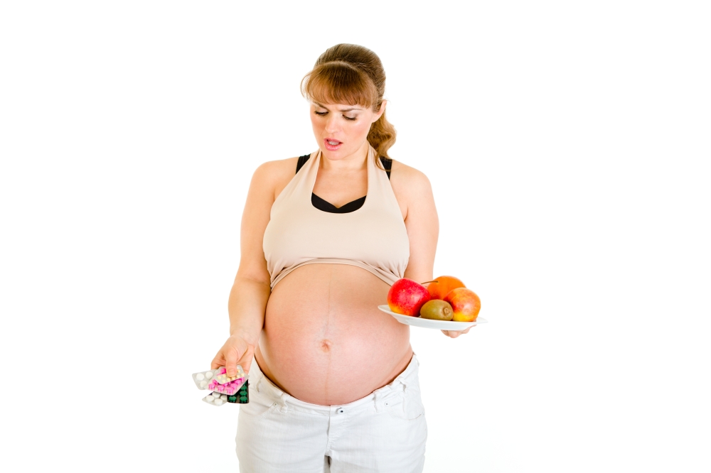 Thoughtful pregnant woman making choice between pills and fruits isolated on white&#xA;