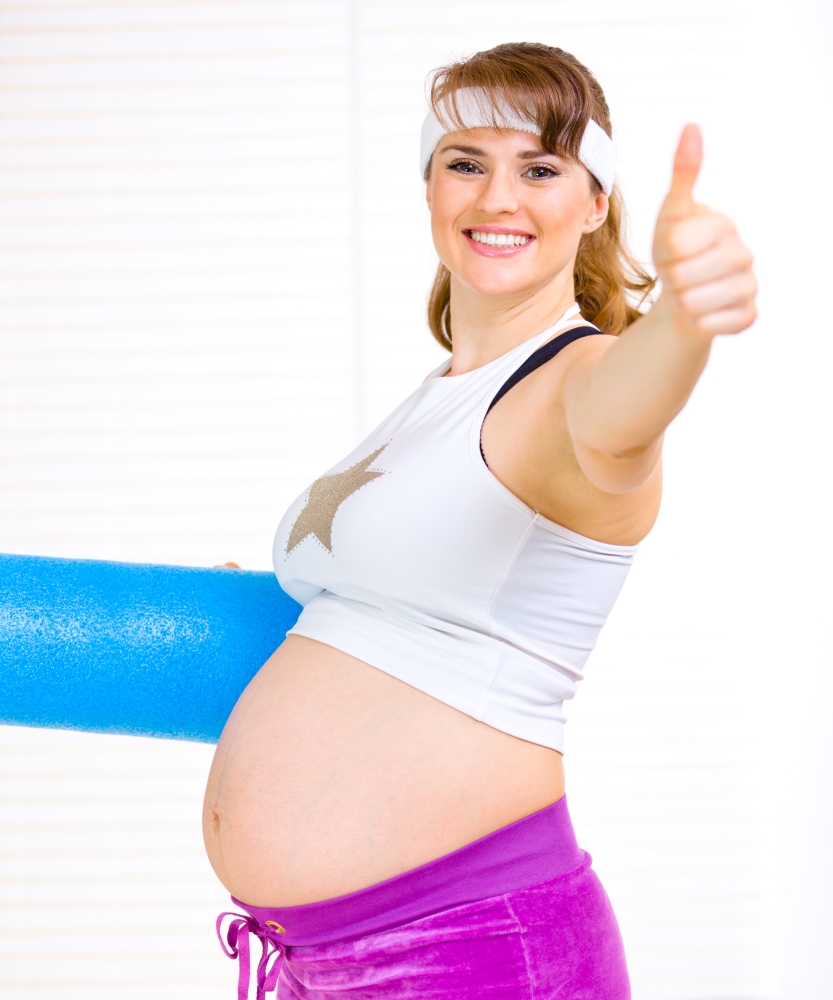 Smiling beautiful pregnant woman in sportswear with exercise mat showing thumb up gesture&#xA;