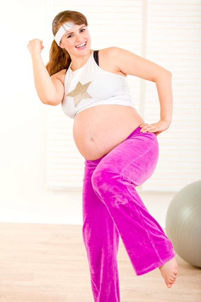 Smiling beautiful pregnant woman doing fitness exercises at living room&#xA;