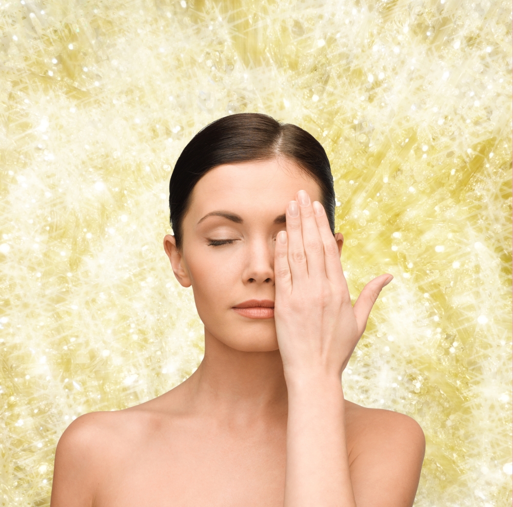 beauty, people and health concept - smiling young woman covering half of face with hand over yellow lights background