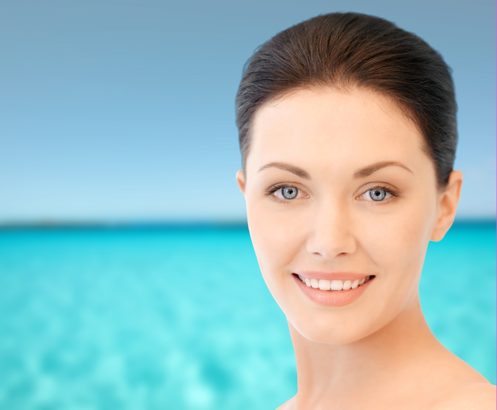 beauty, people and health concept - beautiful young woman face over blue water and sky background