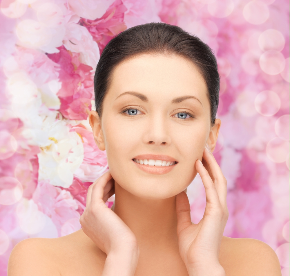 beauty, people and health concept - beautiful young woman touching her face over pink floral background