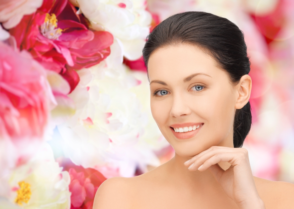 beauty, people and health concept - beautiful young woman touching her face over pink floral background