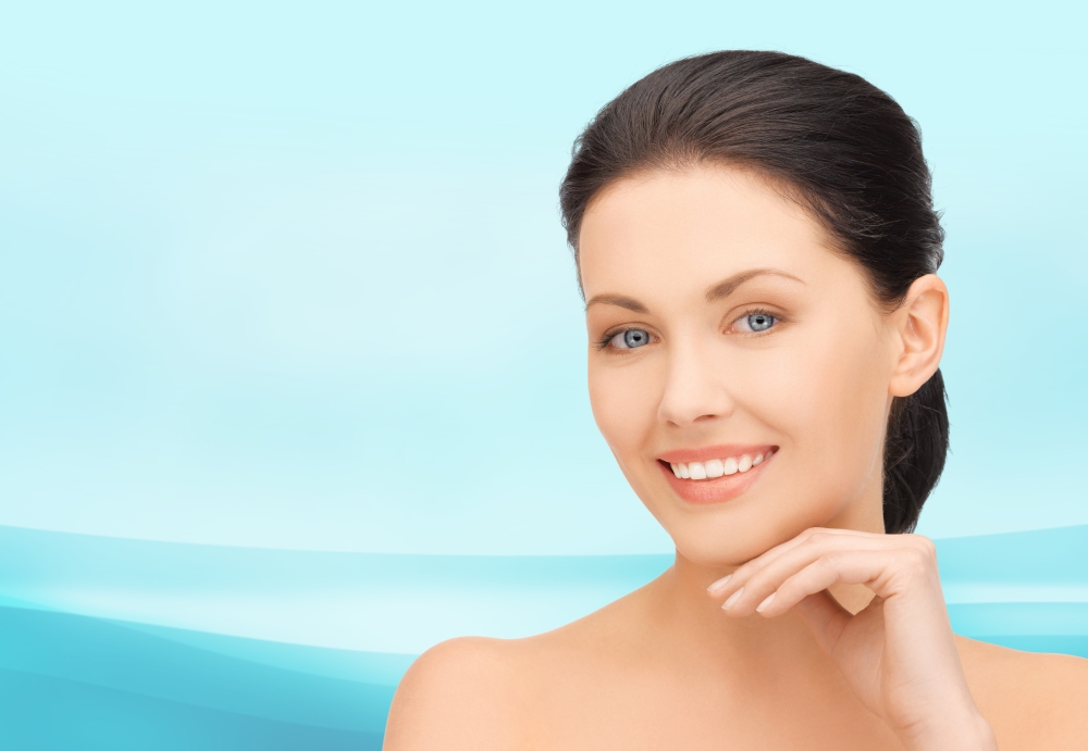beauty, people and health concept - beautiful young woman touching her face over blue waves background