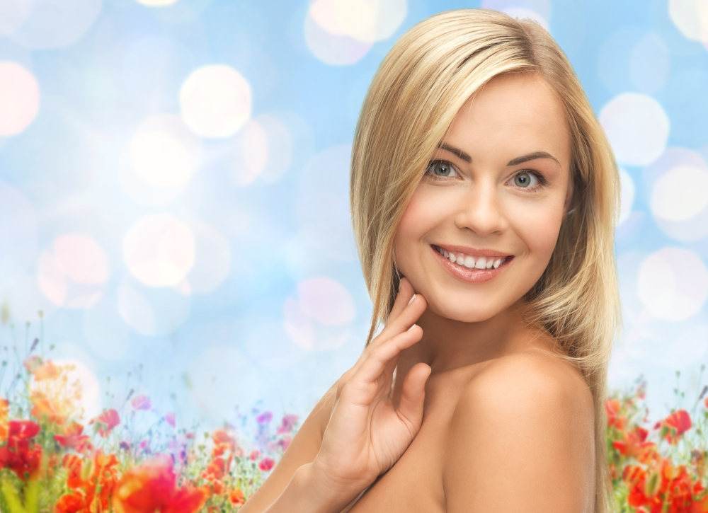 people, beauty, body and skin care concept - beautiful woman face and hands over poppy field and blue lights background