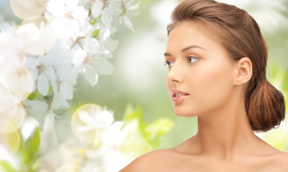 beauty, people and health concept - beautiful young woman face looking aside over green blooming garden background
