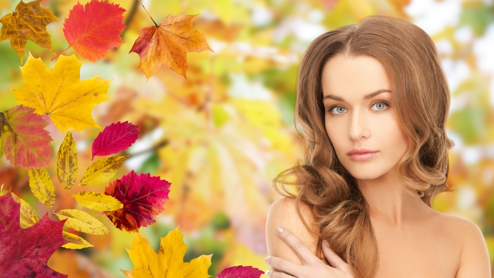 beauty, people, season and health concept - beautiful young woman face with long curly hair over autumn leaves background
