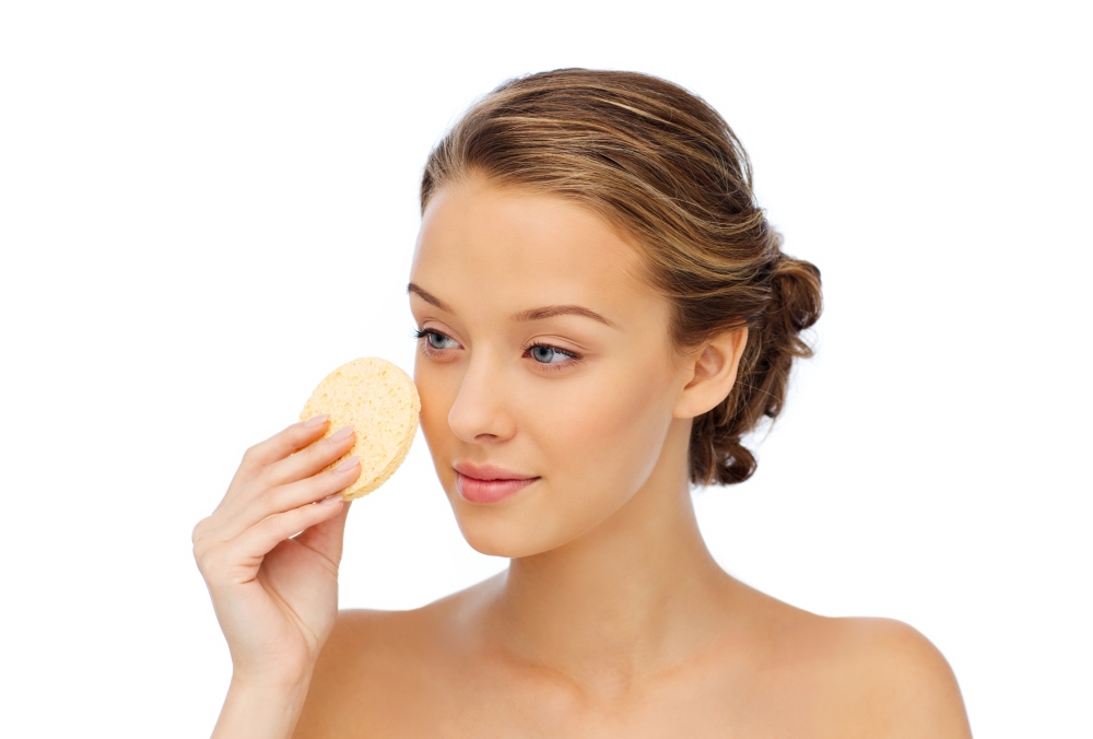 beauty, people and skincare concept - young woman cleaning face with exfoliating sponge