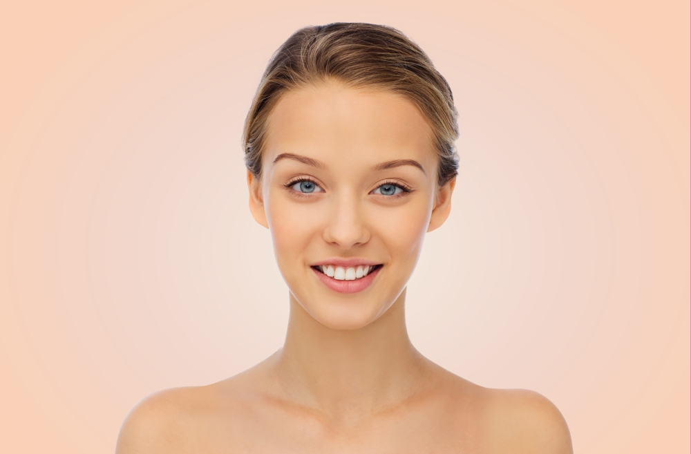 beauty, people and health concept - smiling young woman face and shoulders over beige background
