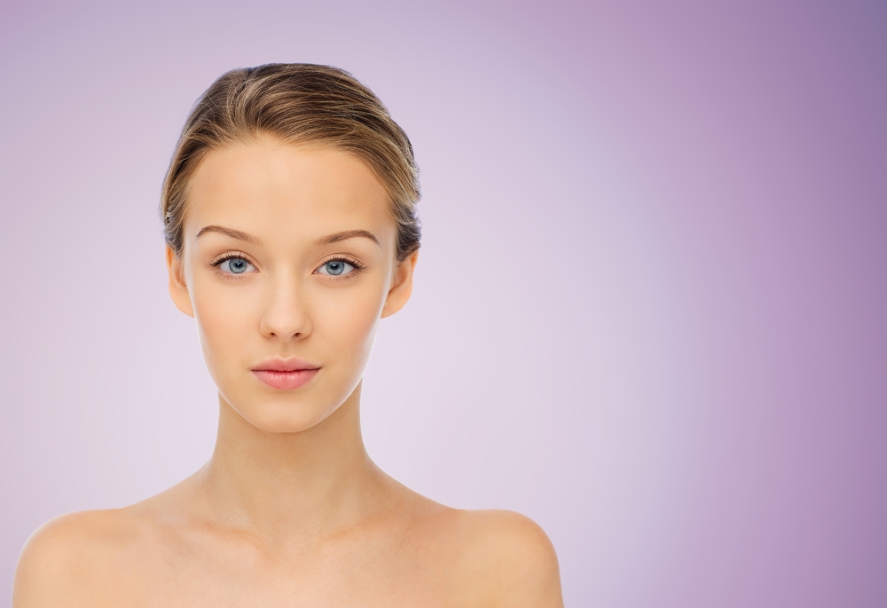 beauty, people and health concept - young woman face and shoulders over violet background