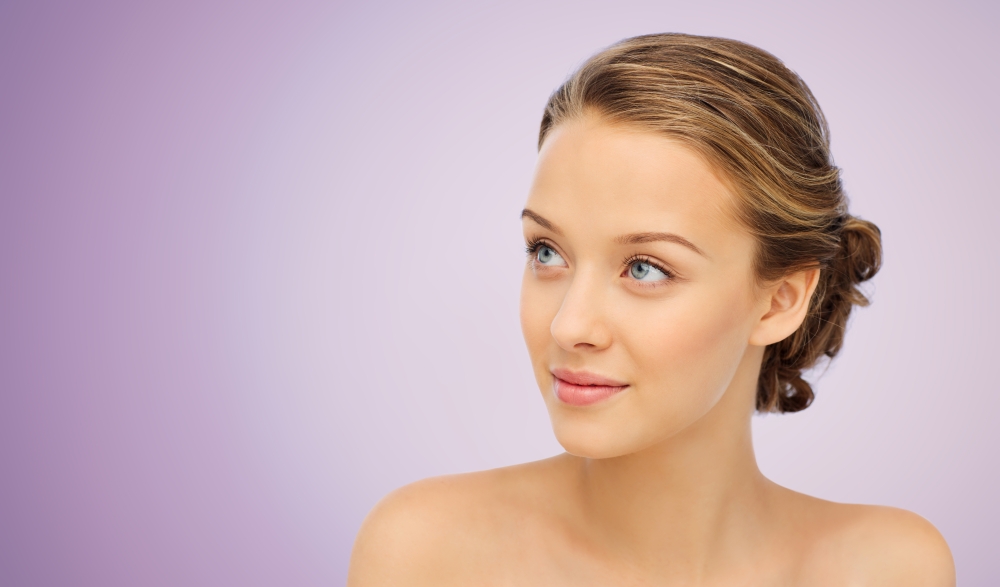 beauty, people and health concept - smiling young woman face and shoulders over violet background